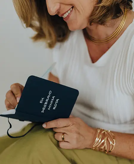 Uma mulher fazendo anotações em um pequeno caderno com a frase Eu desbravo minha rota, gravado na capa