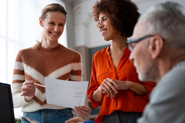 duas mulheres sorridentes e um homem de meia idade, onde uma das mulheres está mostrando um relatório